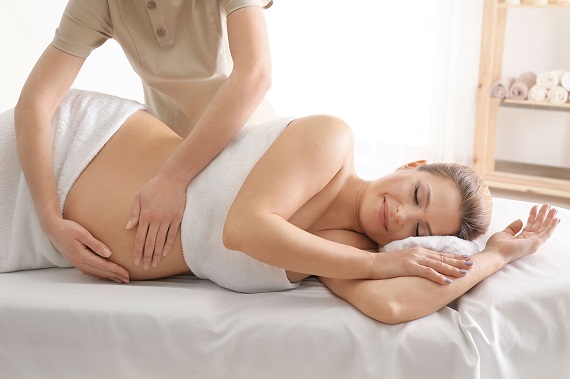 Femme enceinte allongée sur le côté, une masseuse masse le ventre