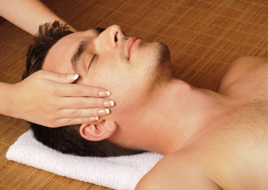 Un homme allongé sur le dos se faison masser le visage