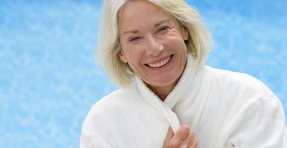 Portrait buste d'une femme en peignoir blanc devant une piscine.