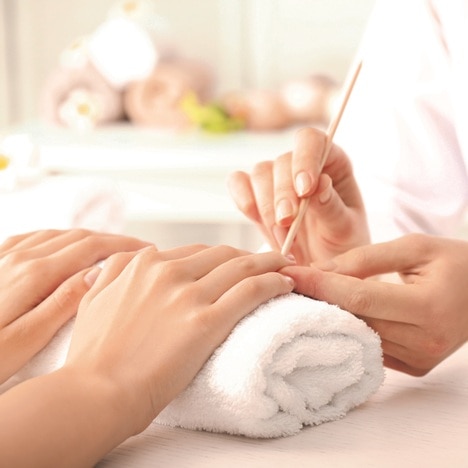 Mains d'une femme en train de se faire une manucure par une esthéticienne.