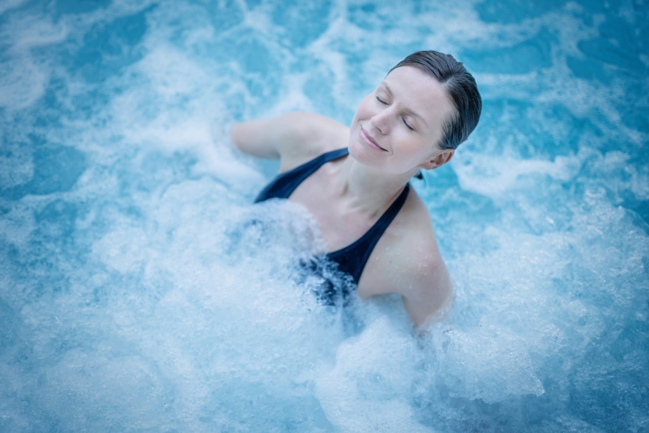 Femme aux cheveux attachés qui se détend dans un bain d'eau de mer chauffée bouillonnant.